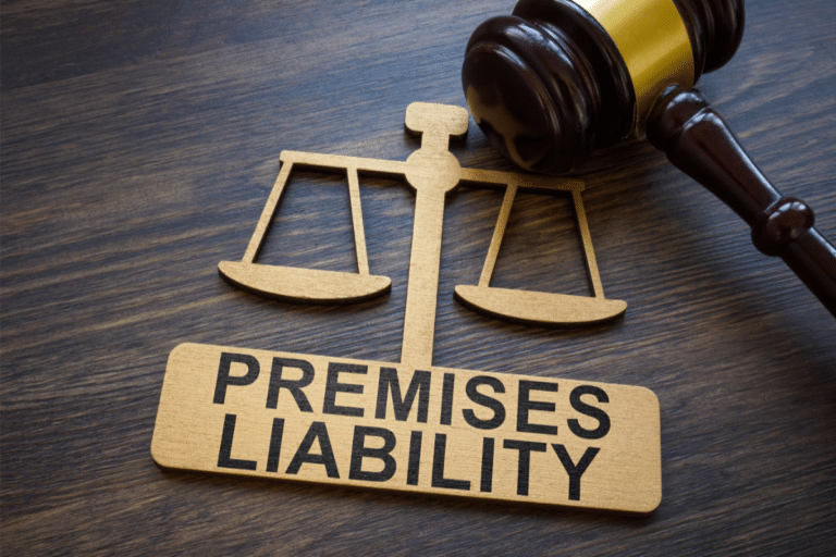 Wooden sign with the words "Premises Liability," a gavel, and scales of justice on a dark wood surface.